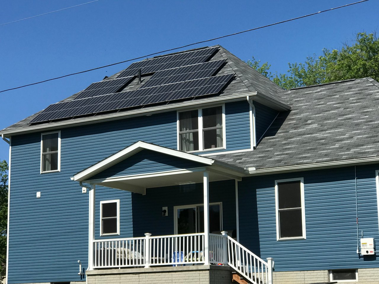 Black solar panels on a blue two-story home with a front porch