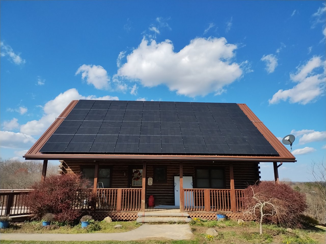 Black solar panels on a log cabin home under a clear blue sky