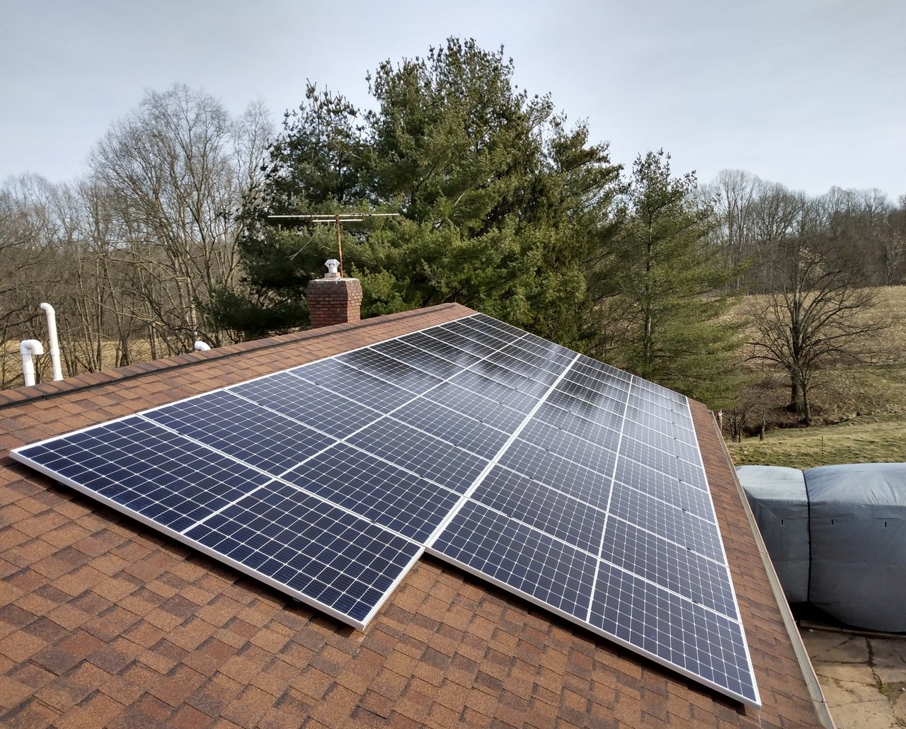Solar array on a shingled roof with a rural winter backdrop